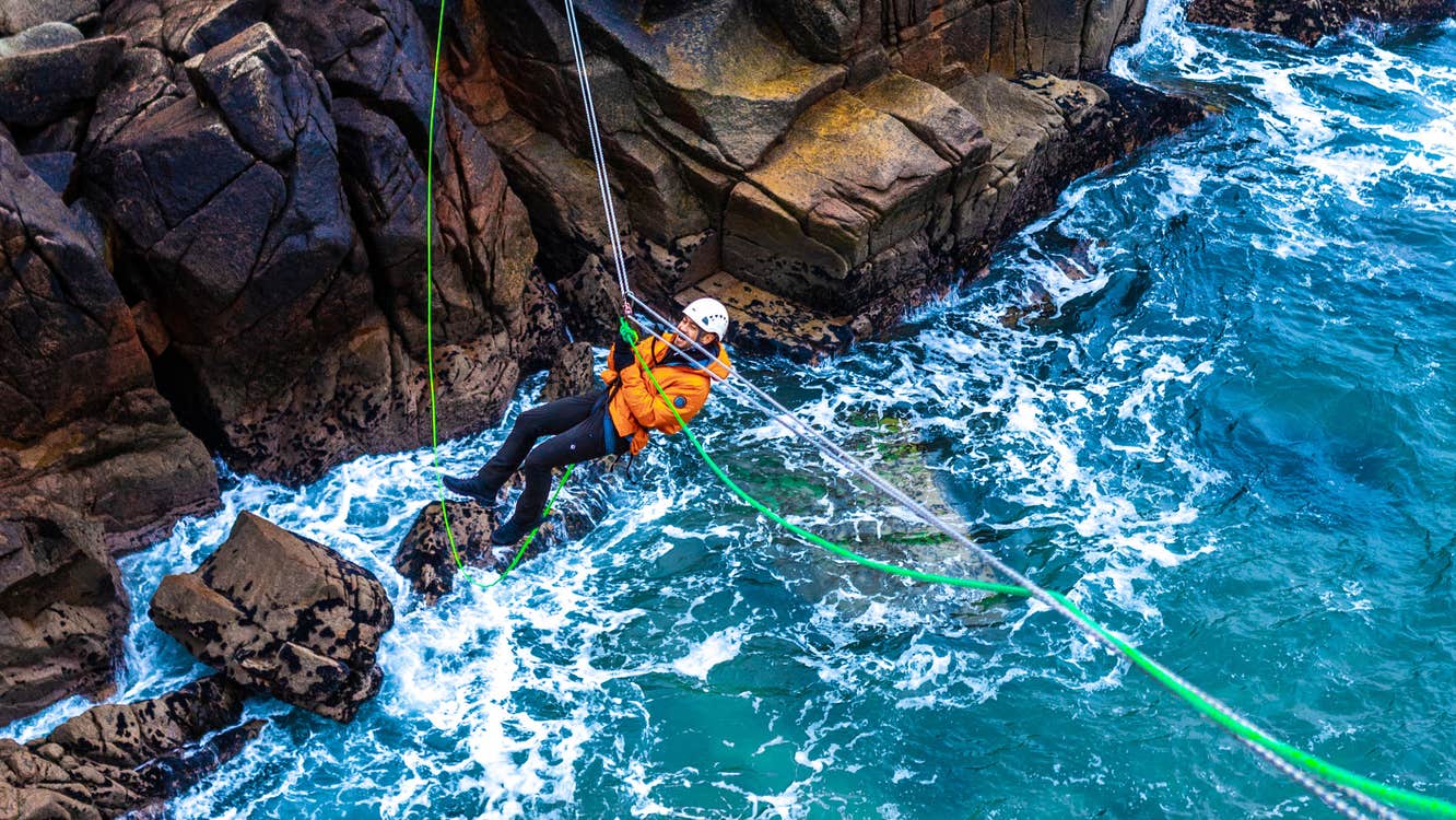 Climber crossing a Tyrolean Traverse rigged above the sea, Cruit Island, County Donegal