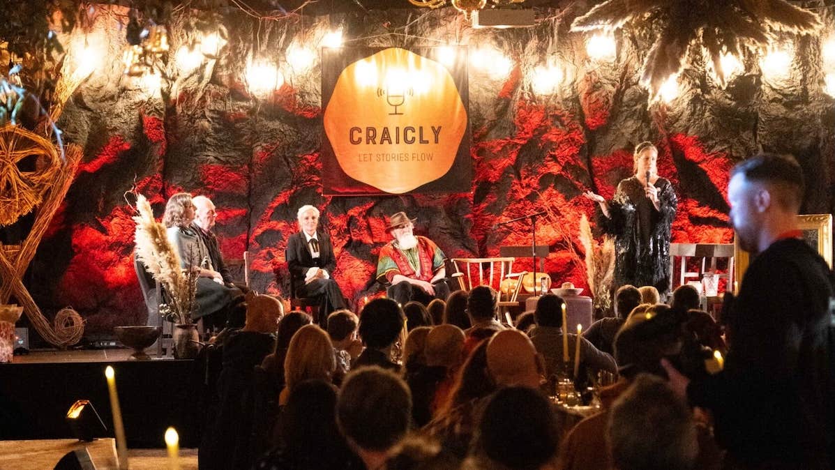 Puca Festival: Craicly Stories, a room with people seated at long dinner tables, looking towards people seated on small stage