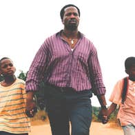 A determined looking man is walking along a road holding the hand of 2 young boys either side of him.