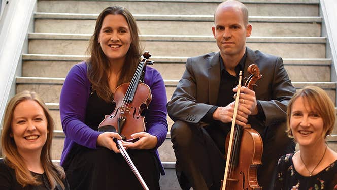 Smiling group of 4 seated on stone steps holding violins