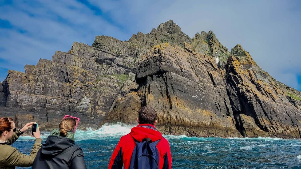 Three passengers on a tour boat taking photos of Little Skellig island