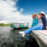 Two people wearing hats relaxing beside a river and boat in Portumna, Co. Galway in Ireland's Hidden Heartlands.