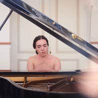 Looking through the open lid of grand piano at a woman playing at the keyboard.