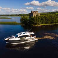 A boat on a large lake beside a small island with a castle surrounded by trees