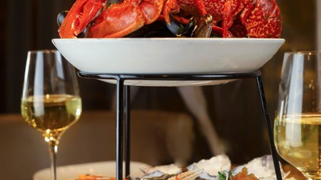 A tiered plate of lobster and lobster tails with two white wine glasses in the background