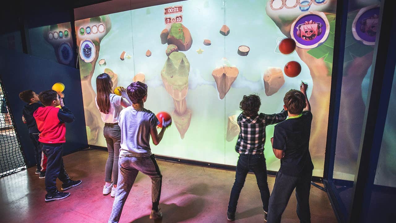 Children in a gaming room throwing balls at an interactive wall