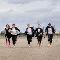 musicians running on Dollymount Strand with the Poolbeg Towers and blue skies behind them