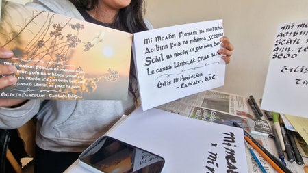 A lady holding two cards with Irish calligraphy on them
