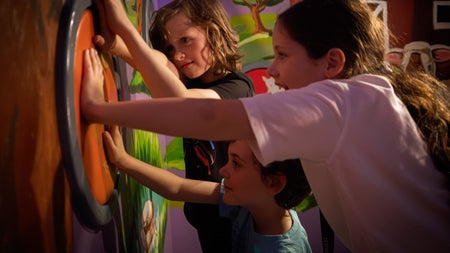 Three children pushing against a wall