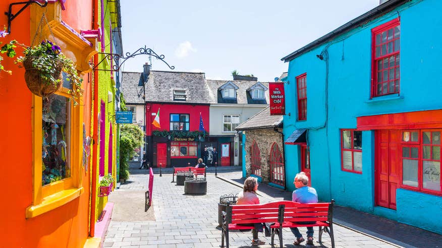 Colourful buildings in Kinsale, Cork with a couple sitting on a red bench.