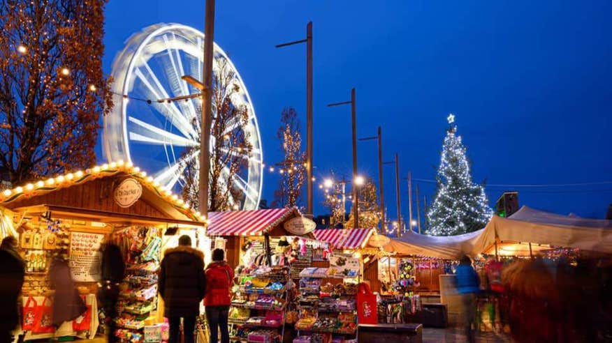 A shot of the Galway Christmas Market with people all around and a Ferris wheel lit up with Christmas lights.