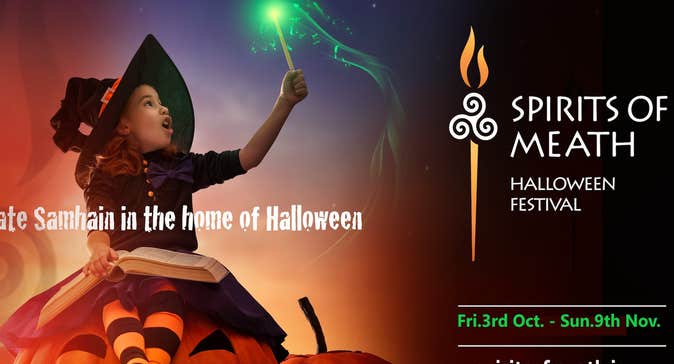 Child in witch's costume sitting on a large pumpkin holding up a wand with a green tip
