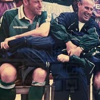 A group of laughing men in football strips seated with another man laid horizontally across their laps also laughing.