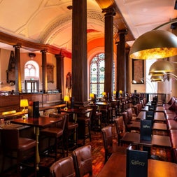 A bar with a seating area in a tall room with stained glass windows