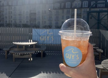 A hand holding up a take away cup with a cold drink from Guy's