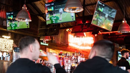 Two people in a pub with a rugby match showing on three screen above the bar
