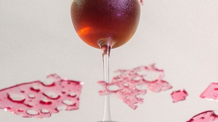 Looking up at a dark coloured cocktail from beneath a glass surface