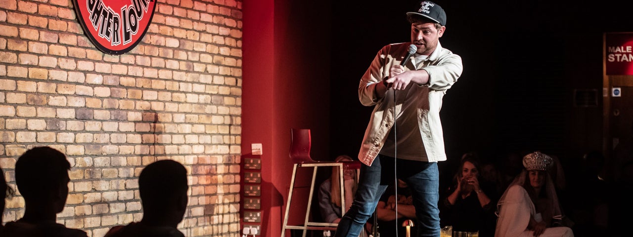 Friday Night Live - Friday, 20th March 2026, a man on a small stage with a mic, pointing at the audience.