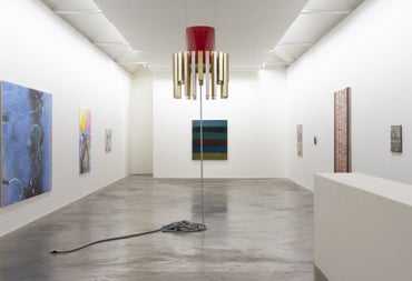 Art gallery displaying a gold and red lamp with an unplugged lead and paintings on the walls