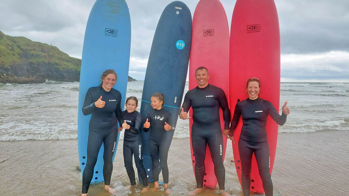 Murfs Surf School family standing in front of surfboards on the beach