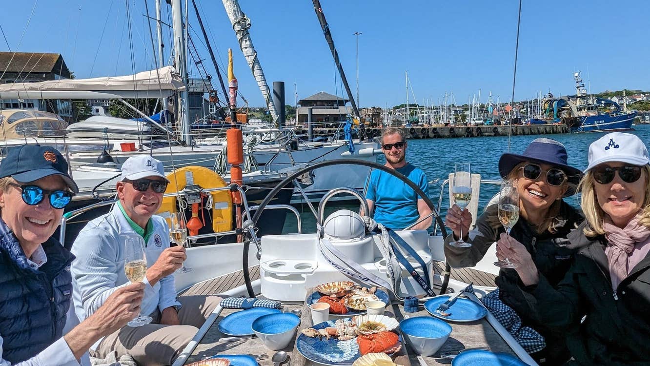 Four people on a yacht sitting around a small table with food platters