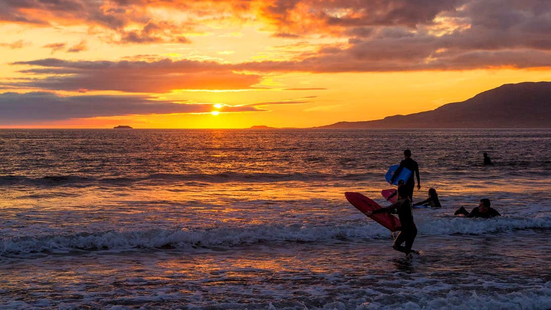 A family walking into the water with surf boards at sunset at Carrowniskey Beach in Mayo.