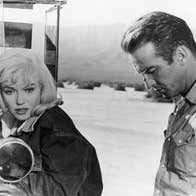 A morose man and woman next to a truck in a desert.