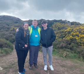 A tour guide and two clients posing for the camera surrounded by whin bushes with hills in the background