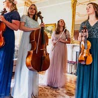 Glas Quartet, 4 women in long evening dresses holding musical instruments in an ornate room.
