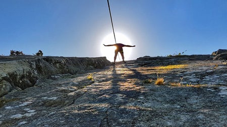 A view taken from the ground looking up at a person abseiling down a rock face