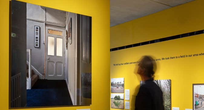 A man viewing photo art hung on a yellow wall and four other images are hanging on a wall behind him