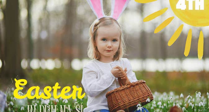 A young girl with rabbit ears headband holding a wicker basket seated on the ground with small white flowers.