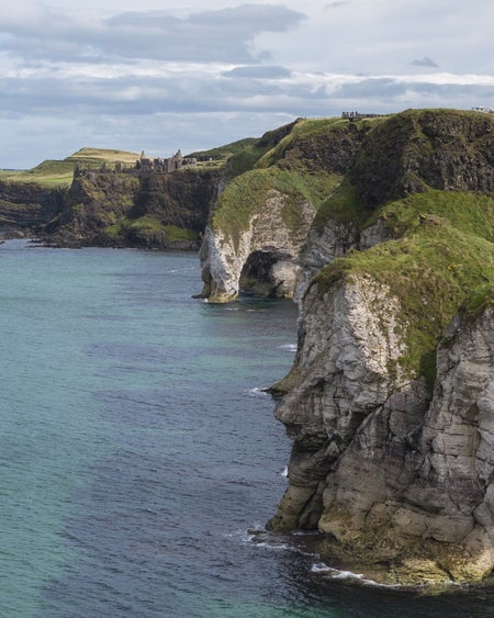 White cliffs with green grass and a faraway castle next to a blue and green coloured sea