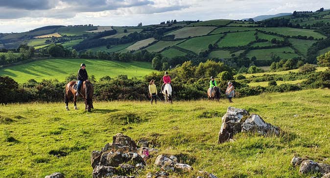 A group on horseback on a trek in a field with rocks on foreground