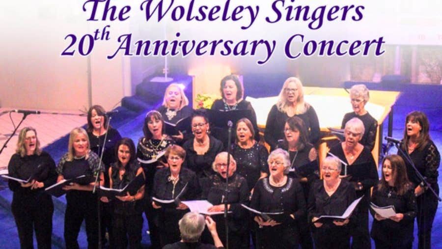 A choir of women holding song sheets, singing with a conductor at the front.