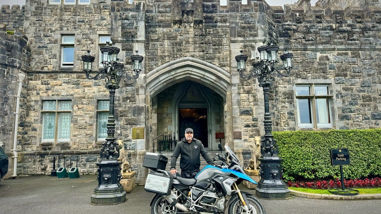 Man posing with a motorbike at a castle entrance