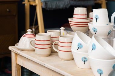 Table display of white glazed pottery with red stripes and some with a tree motif