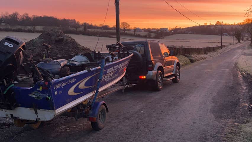 A jeep along the side of a road with a boat on a trailer at a colourful sunset