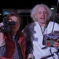 2 shocked looking men, one with a large video camera on one shoulder, the other holding a remote controller.