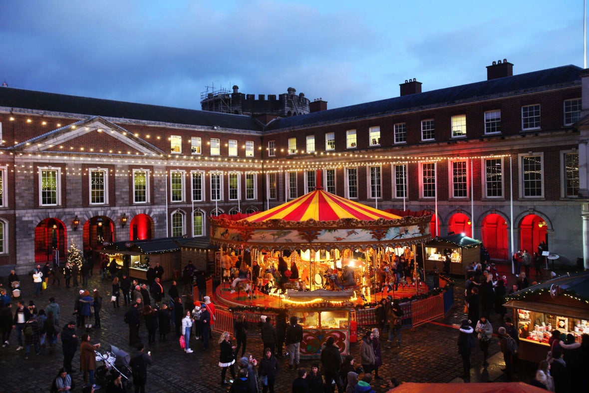 A lit up carousel at dusk in Dublin Castle with fairy lights hung above and people all around.