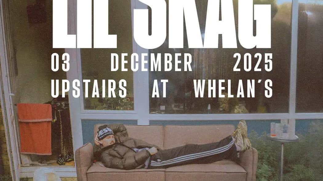 A man is laying on an old brown sofa in front of a building in a scruffy garden