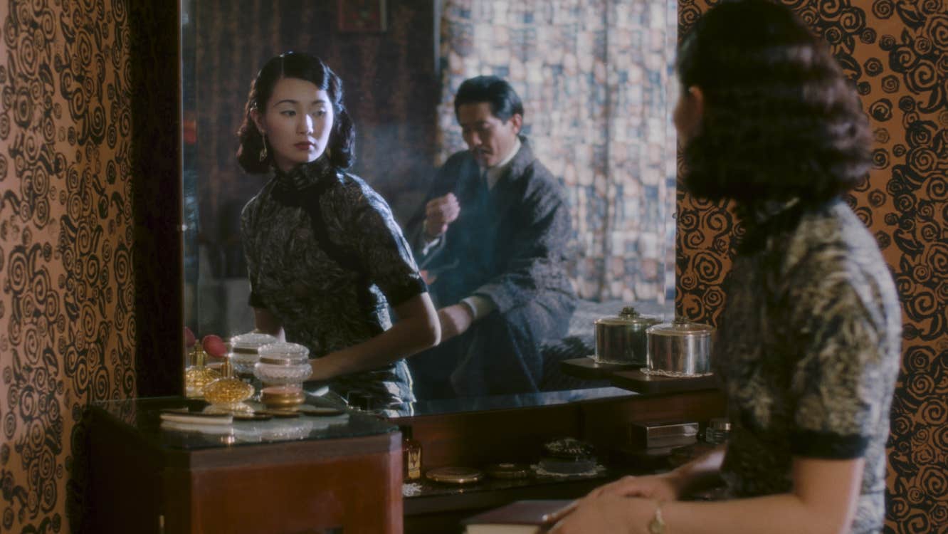 A woman is looking at a mirror. There is a man behind her.