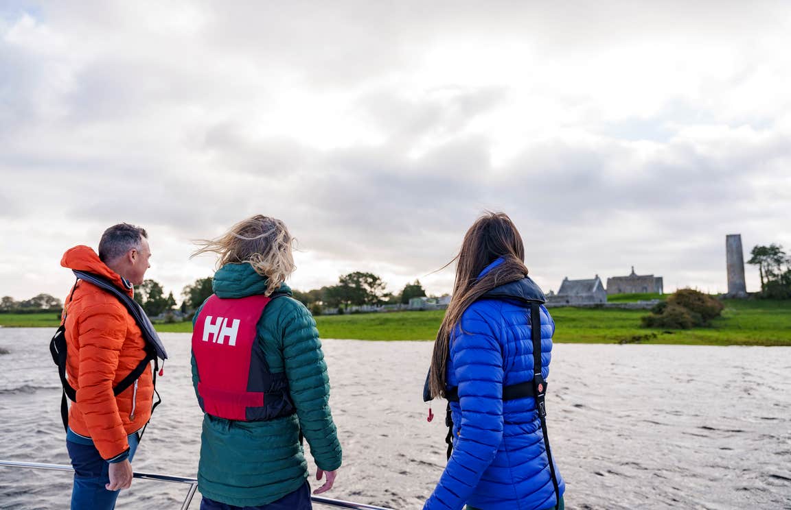 Three people looking out at Clonmacnoise monastic site from a river cruise.