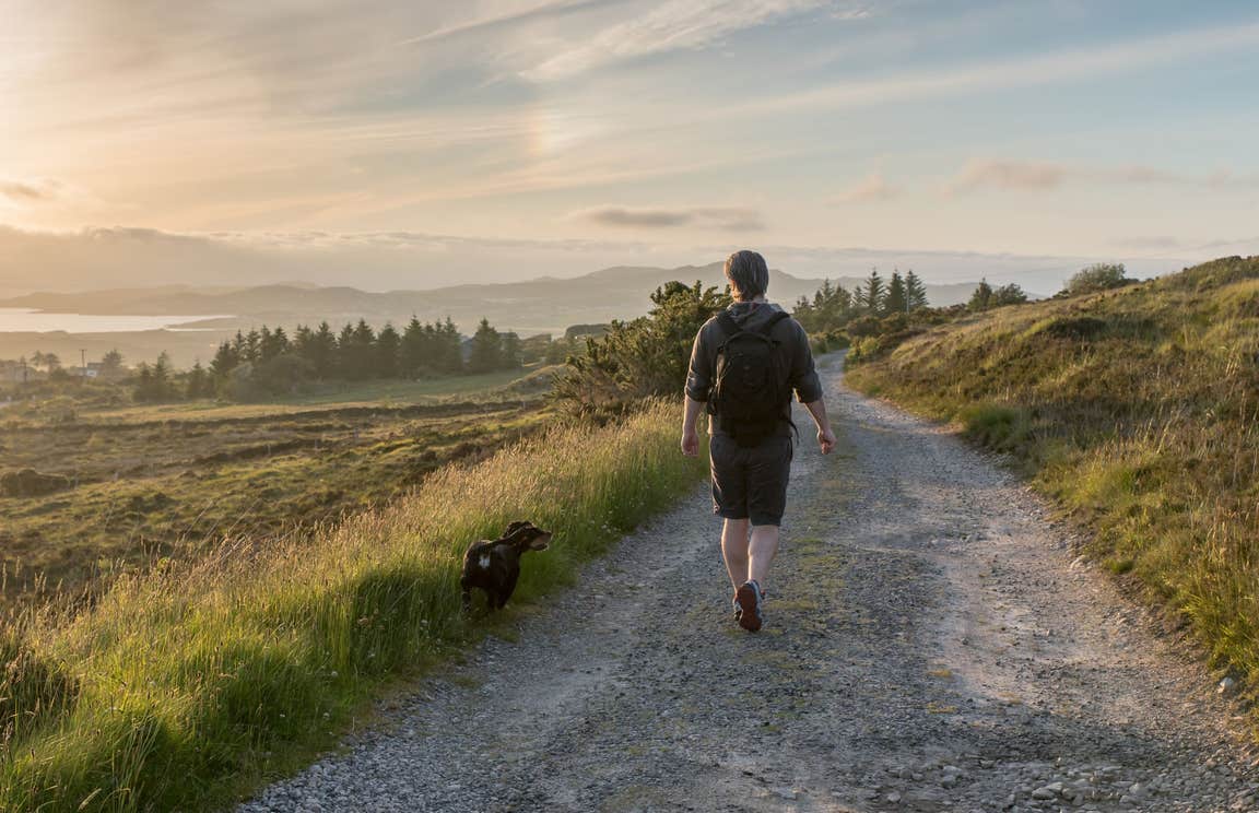 A man and his dog walking in Co. Donegal with views of trees and mountains in the distance