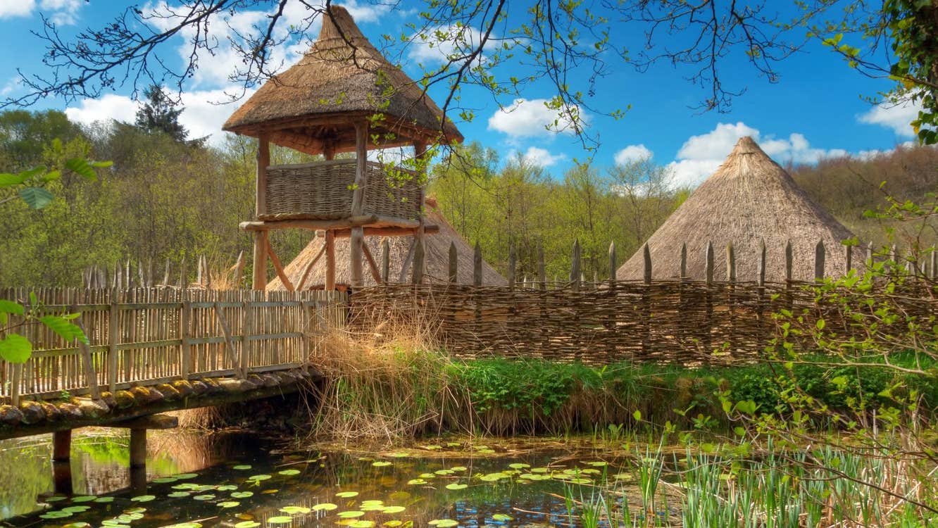 A wooden bridge over a lake with a thatched watch tower