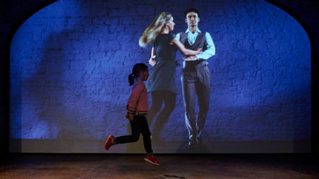 Child dancing in front of a wall with a projected image of two Irish dancers