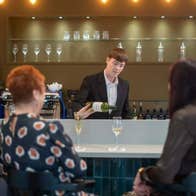 Person serving white wine to three people sitting at the bar
