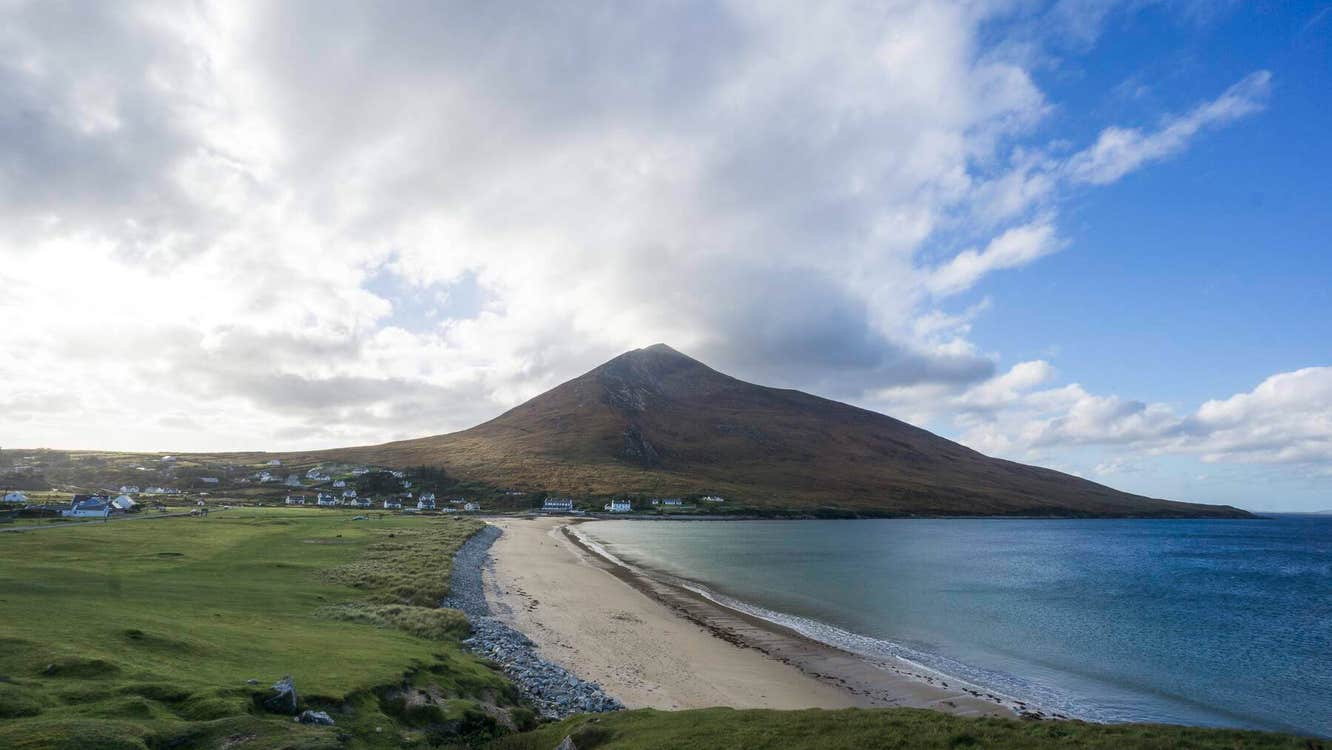 Beach in the forefront with a mountain at the end of the beach