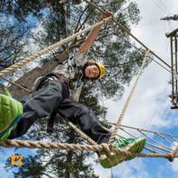 Child looking down at the camera walking on a rope between trees with a blue sky above