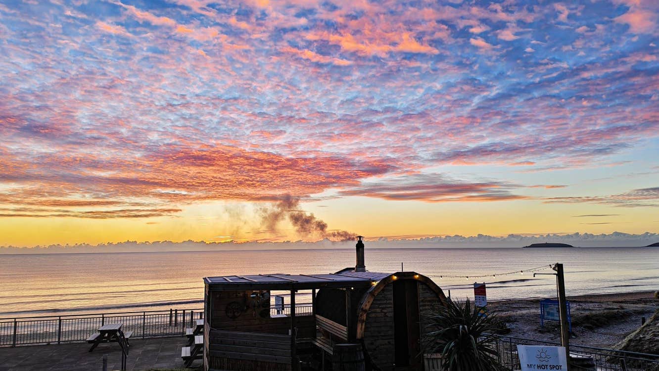 A coastal sauna overlooking a calm sunrise sky filled with pink and orange clouds